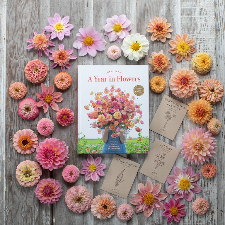An overhead of Floret Farm’s A Year in Flowers book and seed packet surrounded by sherbet colored flowers